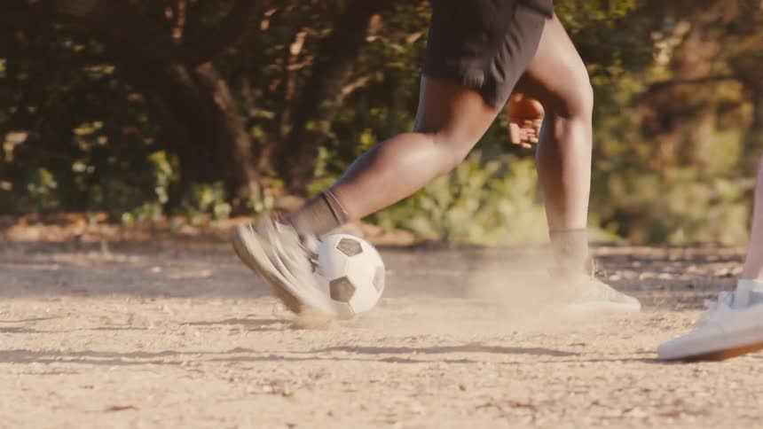 Two young men are happily playing soccer on a dirt floor