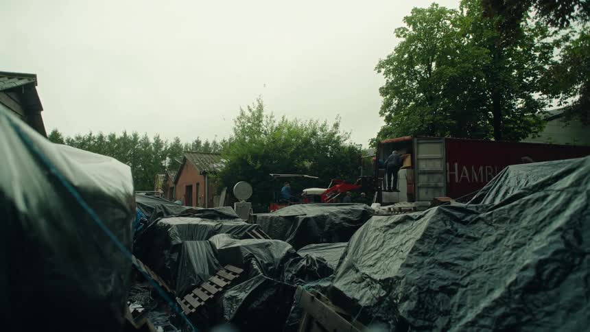 Yard filled with objects covered by tarps with men loading a truck in the background