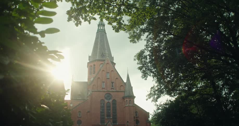 A large church spire with a sunflare through some leaves