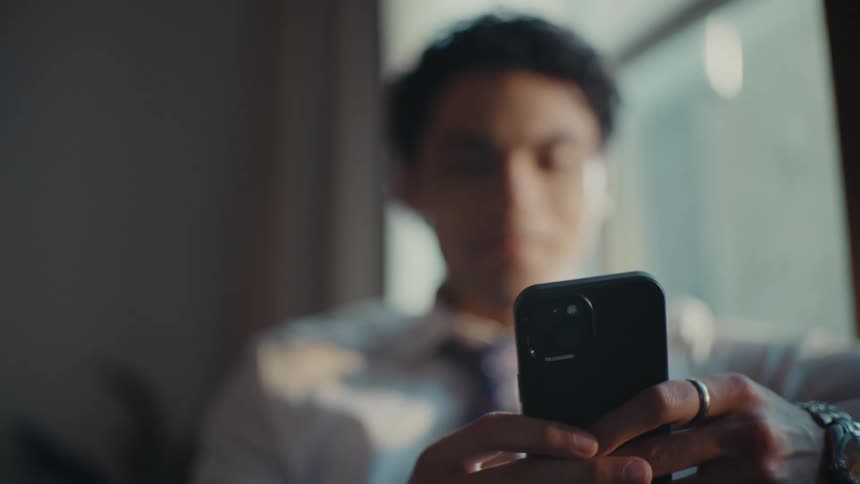 A hispanic man works on his smartphone while sitting indoors