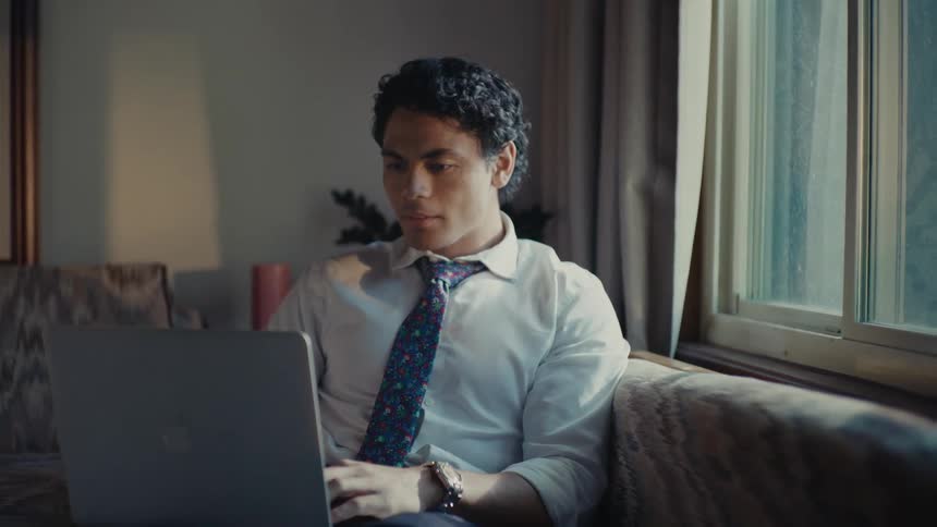 A hispanic man types on a laptop while sitting on his couch