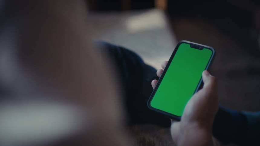 A person holds a smartphone with a green screen in an indoor setting