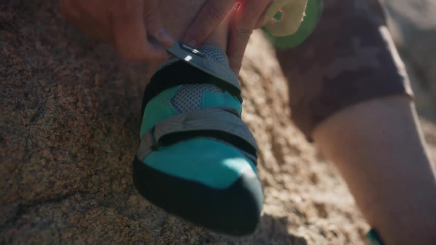 A closeup of a persons hands tying the laces of a climbing shoe on a rocky surface