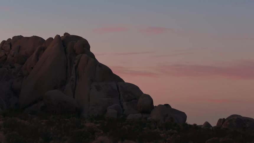 A landscape during twilight with large rock formations against a sky with hues of pink and blue