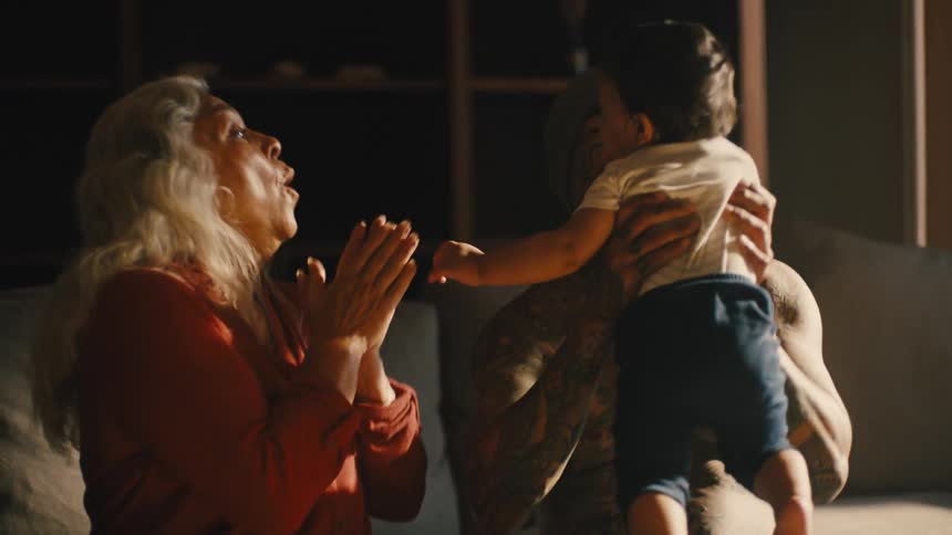 Man holding his son in his arms with his grandmother by his side