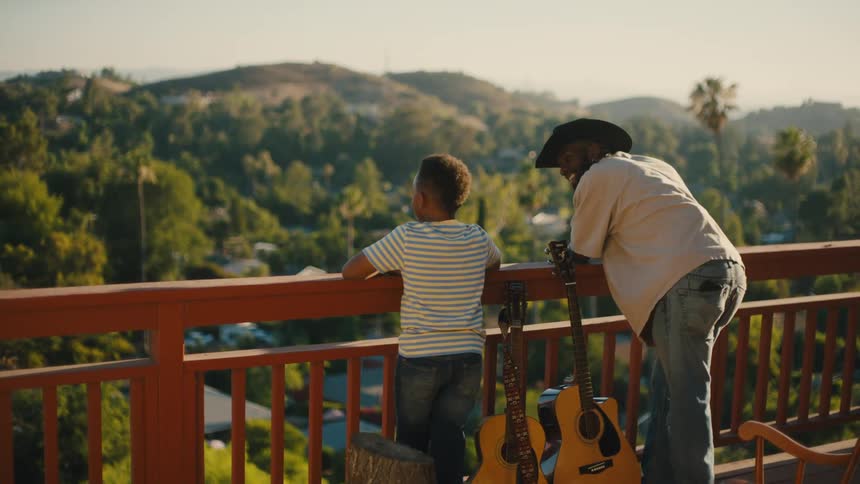 Man next to a boy and with two guitars on a balcony of a building