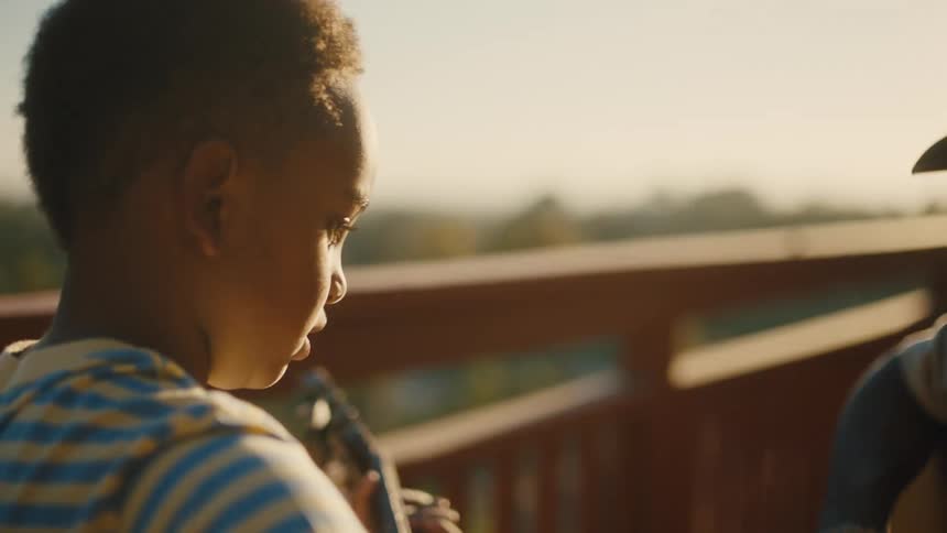 A father sitting playing guitar with his son on a porch as the sun sets