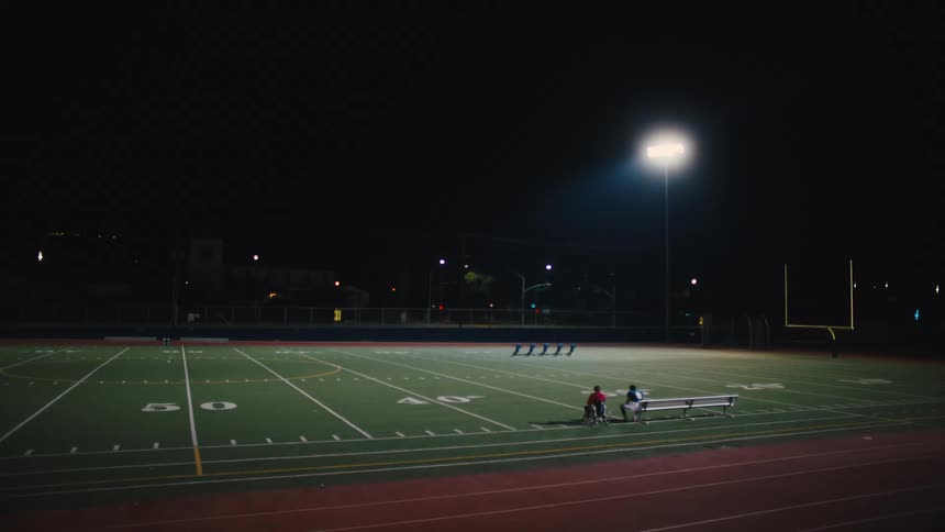 American football field lit up at night and two people sitting