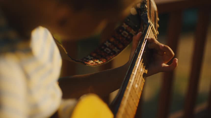 A father teaches his son to play guitar outdoors on a sunny day