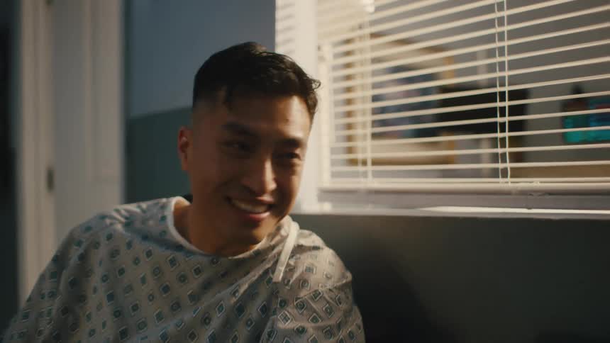 Male patient sitting in hospital gown talking to a nurse in a hospital hallway