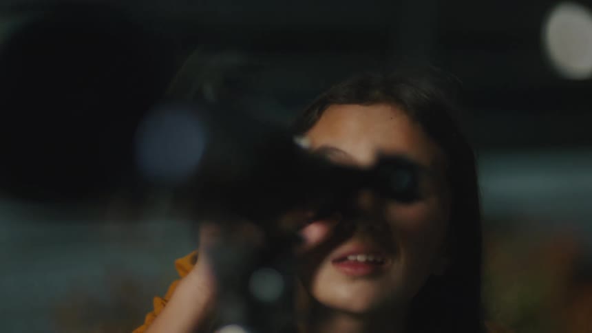 Mother and daughter looking through a telescope at night with blurred city lights in the background