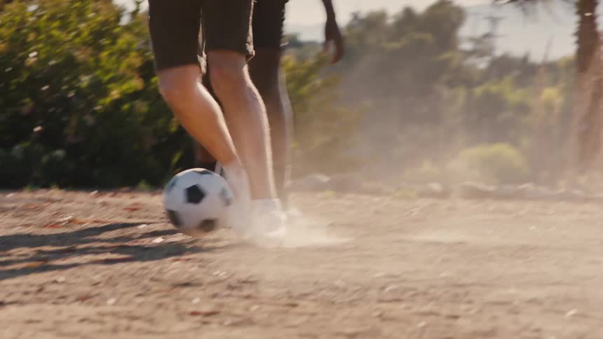 Two teenage boys are playing soccer outdoors on a windy summer day