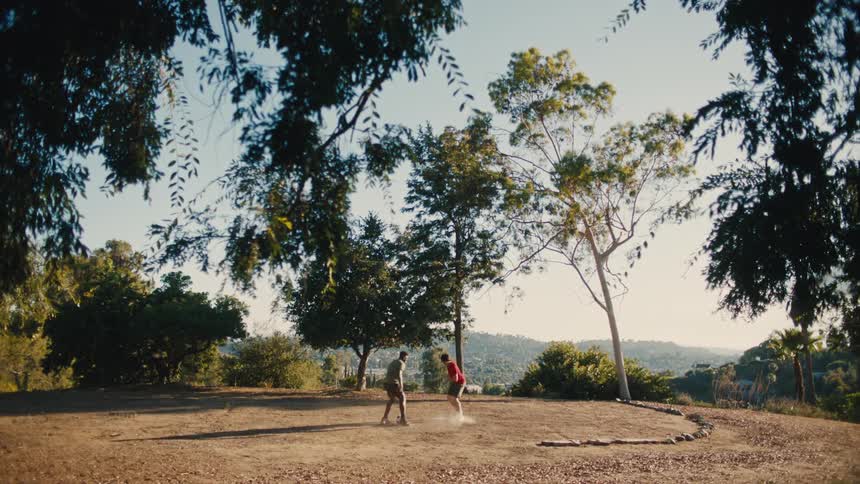 A father and his teenage son kick a soccer ball back and forth atop a mountain