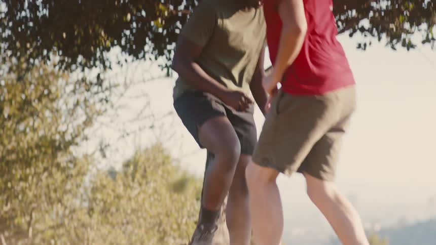 Two boys playing soccer together on a dirt area on a sunny day