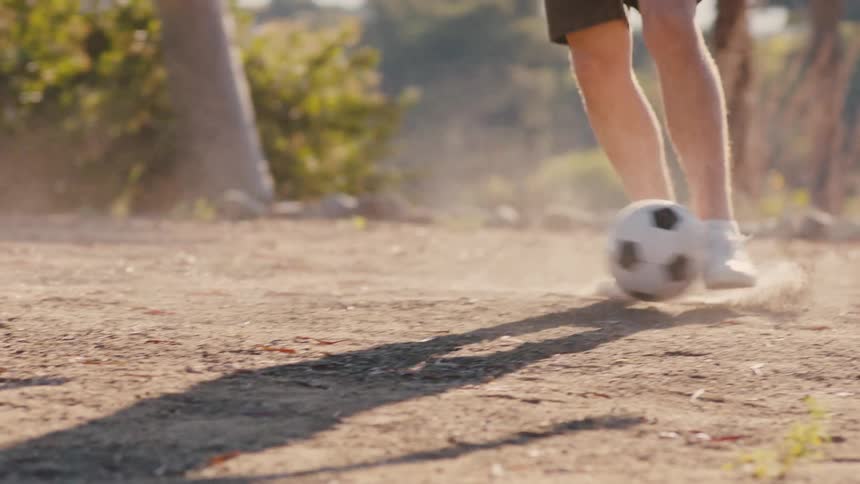 Legs of two teenagers playing soccer on a dirt street
