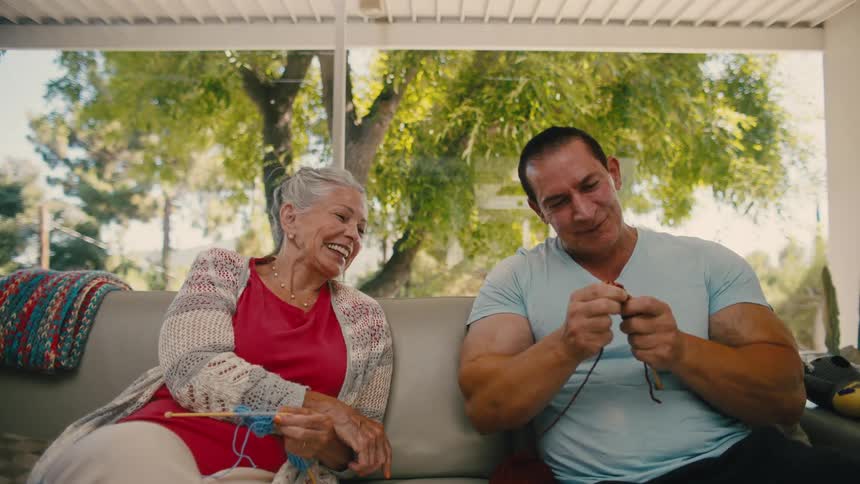 Man next to an elderly lady trying to knit