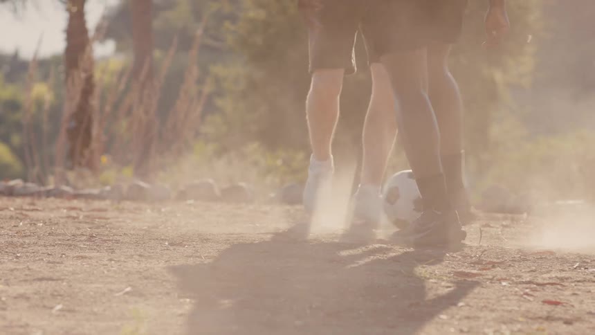 Close up of legs of two young men playing soccer on a dirt road
