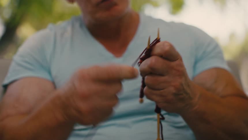 Closeup of a persons hands knitting with brown yarn