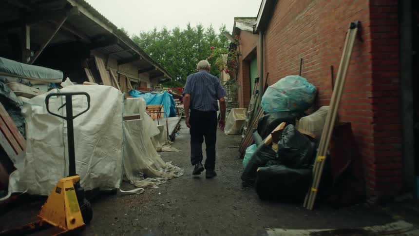 Rear view of an elderly man walking through a cluttered outdoor hallway