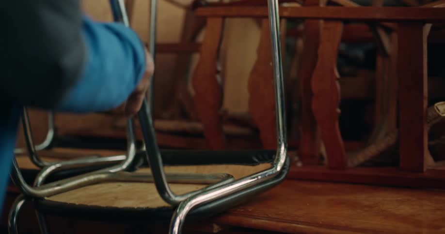 A person stacking a chair upside down on top of furniture