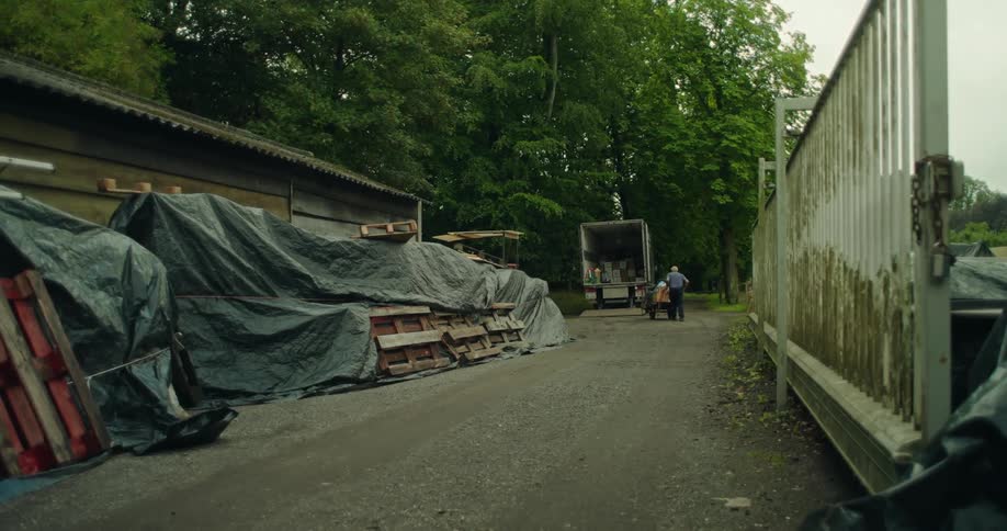 An elderly person pushes a cart towards the back of a truck in a yard