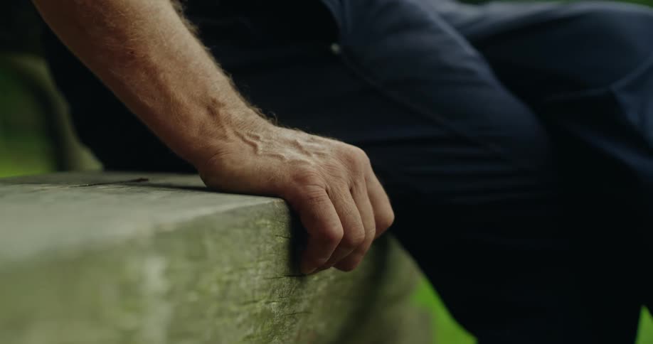 Close up of a mans hand leaning on a wooden bench