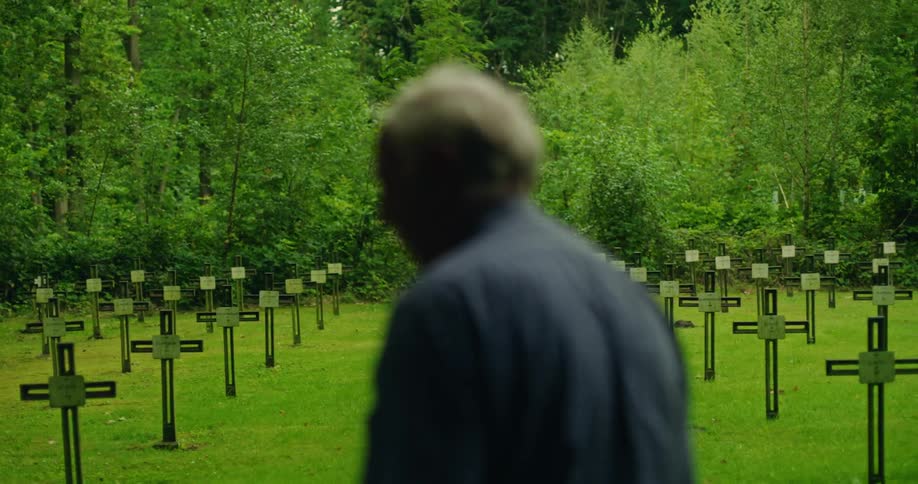 The backside of a man looking at crosses in a cemetery before he walks away