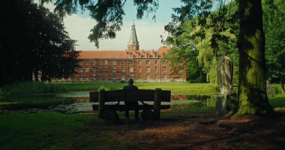 Back view of a man sitting in a chair facing a lake with a monastery in the background