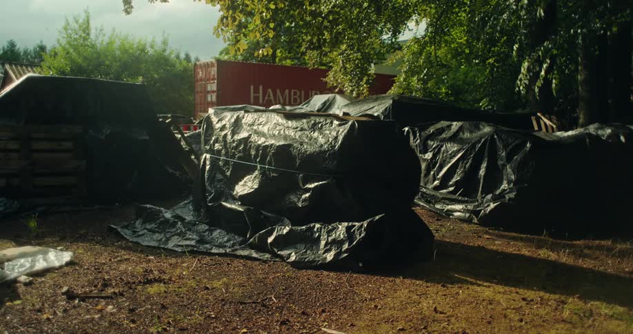 Large objects covered with black tarp tied around them next to a cargo container