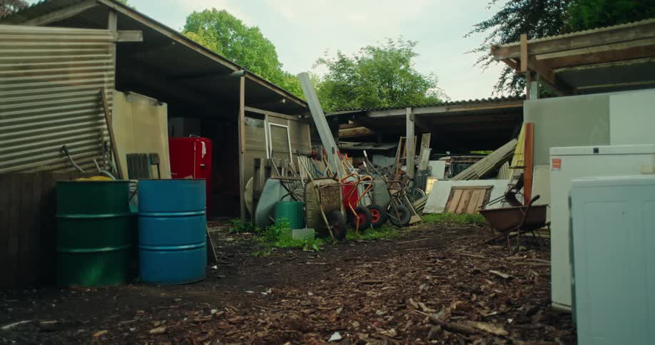 Wheelbarrows stacked on top of each other outside a shed near barrels and other equipment