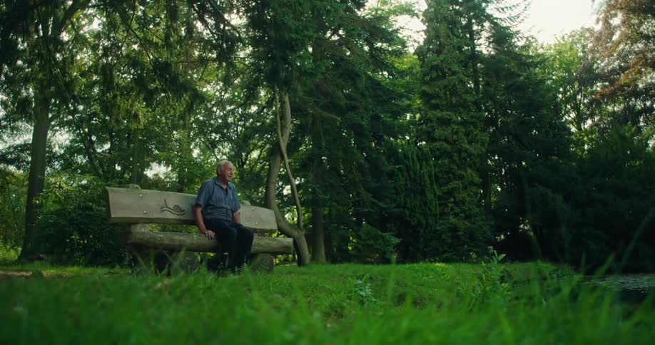 Elderly man walking and sitting on a wooden bench in a forest with trees around