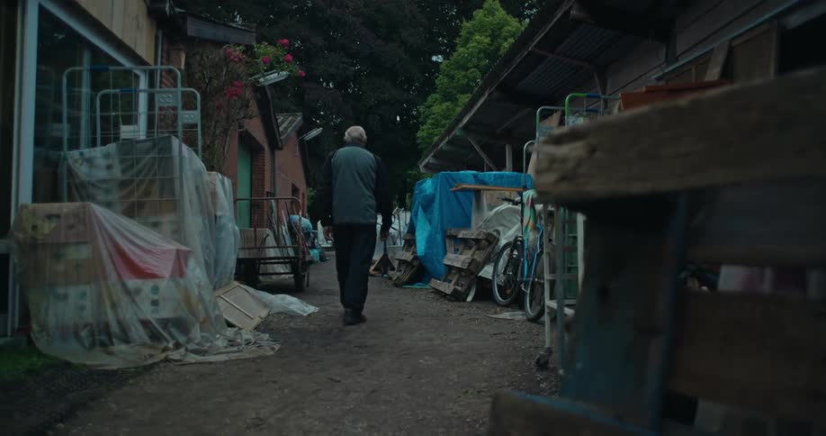 Elderly man walking down an outside hallway with debris