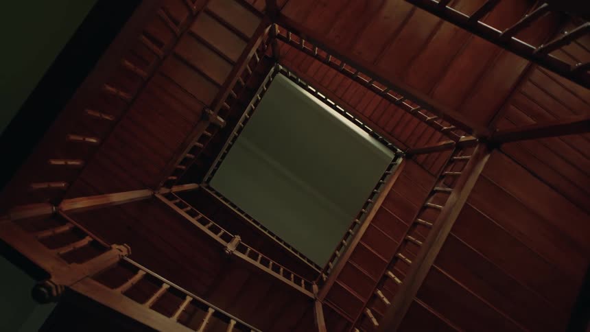 A view looking up from the bottom of a square wooden staircase creating a geometric spiral pattern