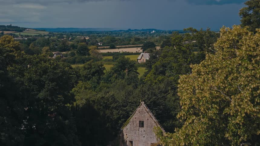 A rural landscape with a historic building nestled amidst dense woodland overlooking a valley