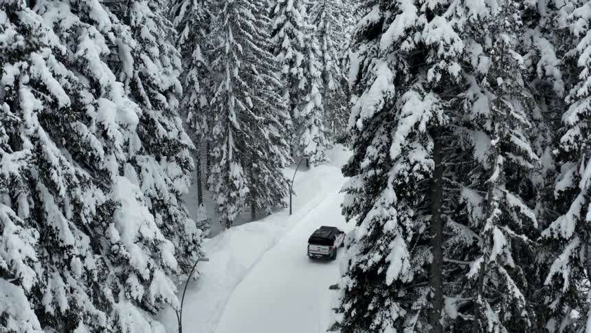 A truck drives on the snow filled road through the forest
