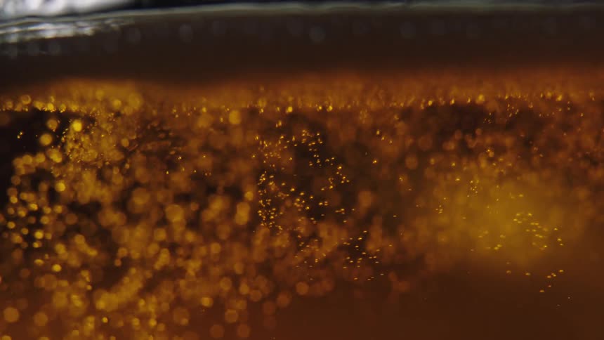 Closeup view of bubbles and foam in a goldenbrown liquid with light reflecting through it creating an amber glow