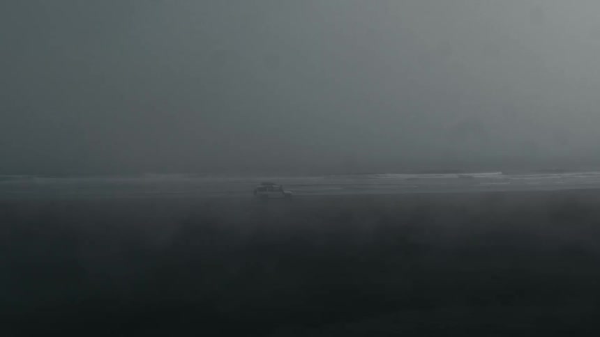 Suv rolling along a beach on a very overcast day
