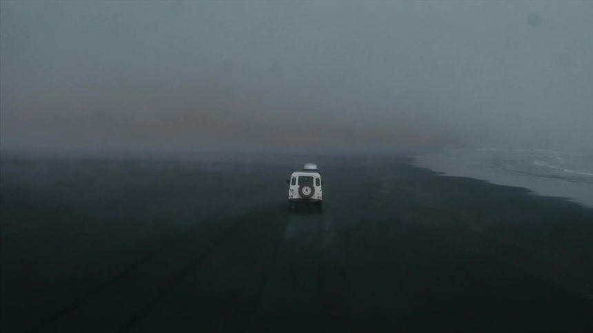 A vehicle drives on a foggy beach