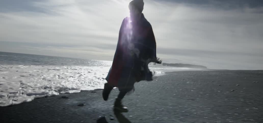 Woman wearing a shawl running playfully from the waves coming ashore