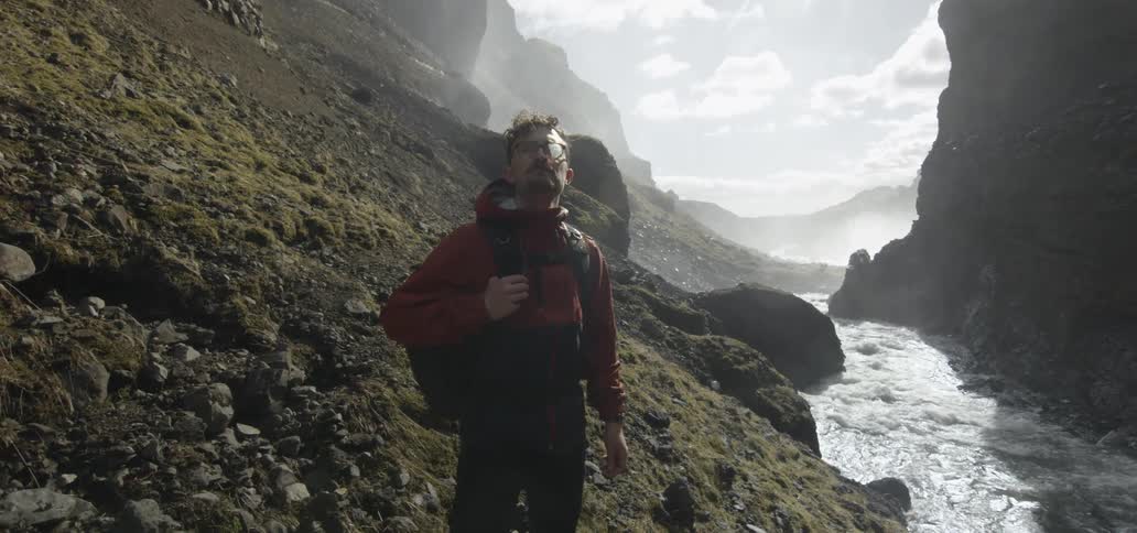 A man with a backpack is standing next to a mountain looking around