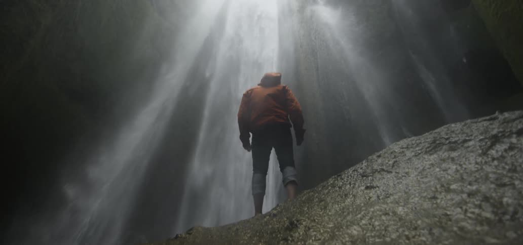 A man stands at the bottom of a waterfall
