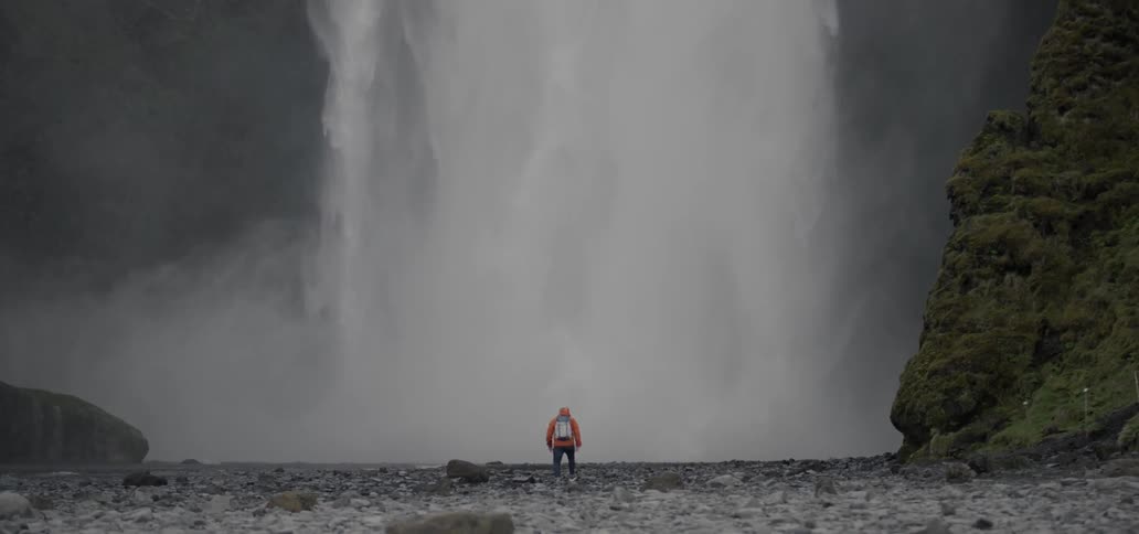 A man walks towards a large waterfall