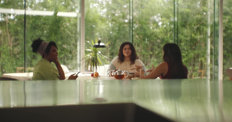 Three women sitting around a table eating drinking tea and talking
