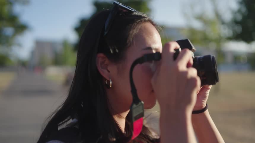 A woman walking on a park with a photo camera stops and takes a photo