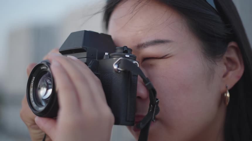 A young asian woman with a professional camera is taking pictures and then takes the camera away from her face
