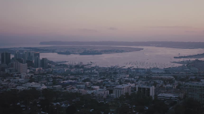 Airplane flies low over a waterfront city as red tints the sky