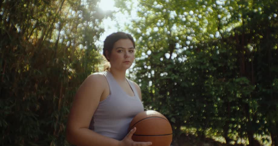 A woman sits in a wheelchair holding a basketball outdoors on a sunny day