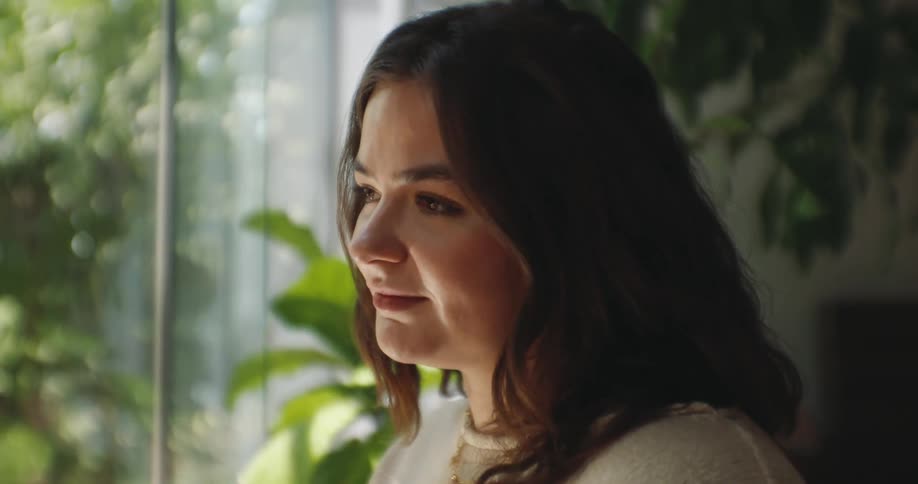 A young woman with long dark hair looks down thoughtfully then looks forward and smiles