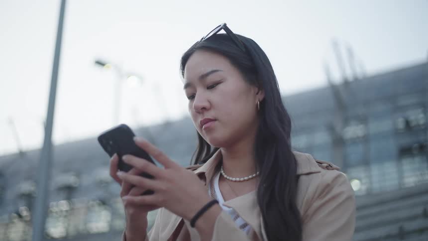 Close up of a woman holding and looking at her cell phone as she looks up contemplatively