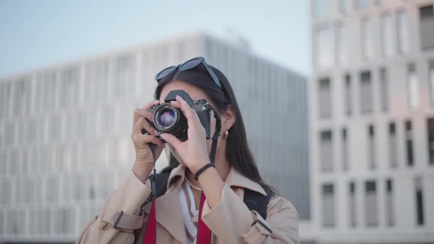 A woman with her back to large modern buildings taking photos